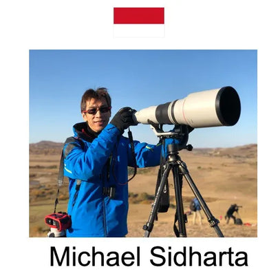 Person holding a large telescope in an open field with a clear blue sky.