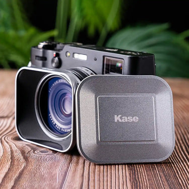 Camera with lens cover and 'Kase' branding on a wooden surface with blurred greenery in the background