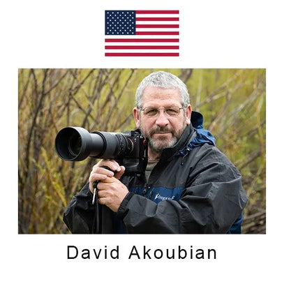 Man holding a camera with a lens, standing outdoors with an American flag in the background