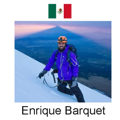 Person in purple jacket and helmet on a mountain peak with a scenic view and Mexican flag above.