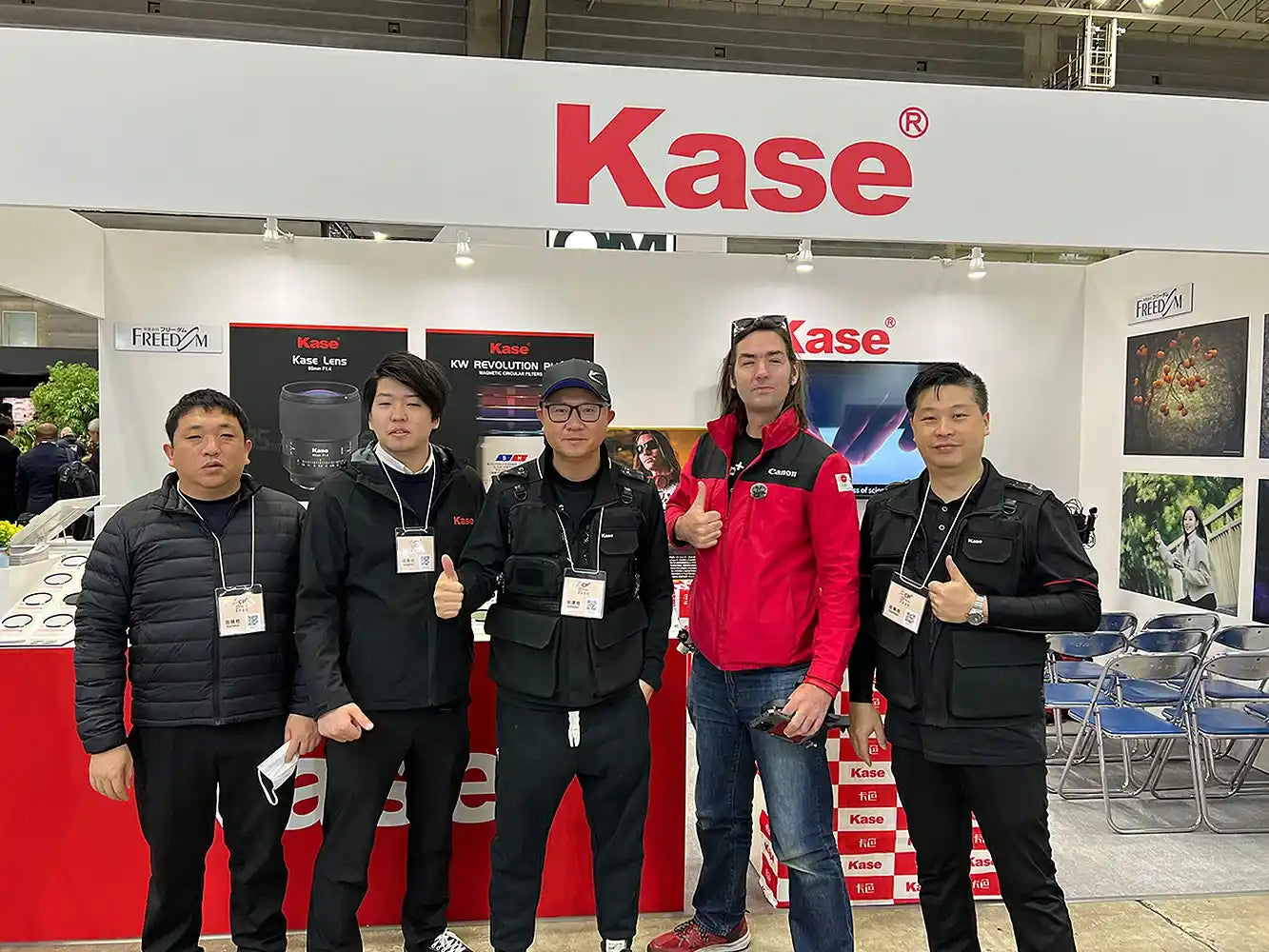 Four team members and a foreign client took a group photo in front of the Kase brand booth.