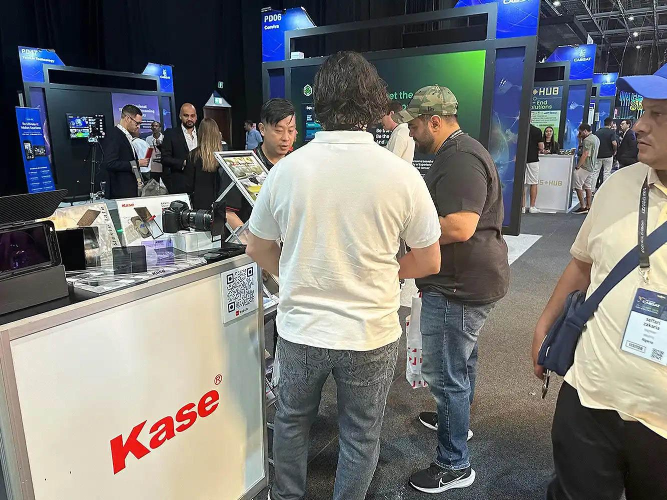 People at a trade show or exhibition with a Kase brand booth.