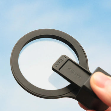 a hand holding a Kase circular optical filter (typically used for phone lenses), with a bright blue sky as the backdrop.