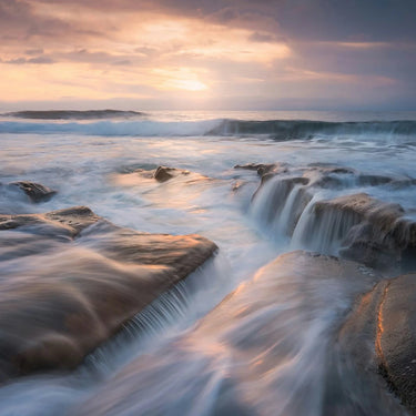 Sunset over a rocky coastline with waves crashing against the shore.