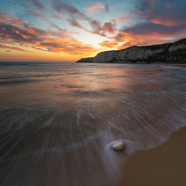 Sunset over a beach with waves and cliffs in the background